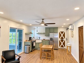 A modern kitchen with a dining area, a ceiling fan, and a view to the outside.