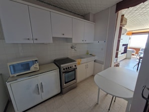 A kitchen with white cabinets, a microwave, a stove, and a sink. - Vrbo Property (Valras-Plage)