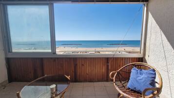 Un balcón con vista a la playa, una mesa de vidrio y una silla de mimbre.