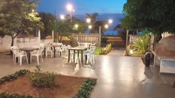An outdoor patio area with tables and chairs, surrounded by plants and a wooden fence.