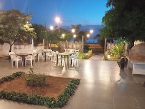 Un'area patio esterna con tavoli e sedie, circondata da piante e un recinto in legno.