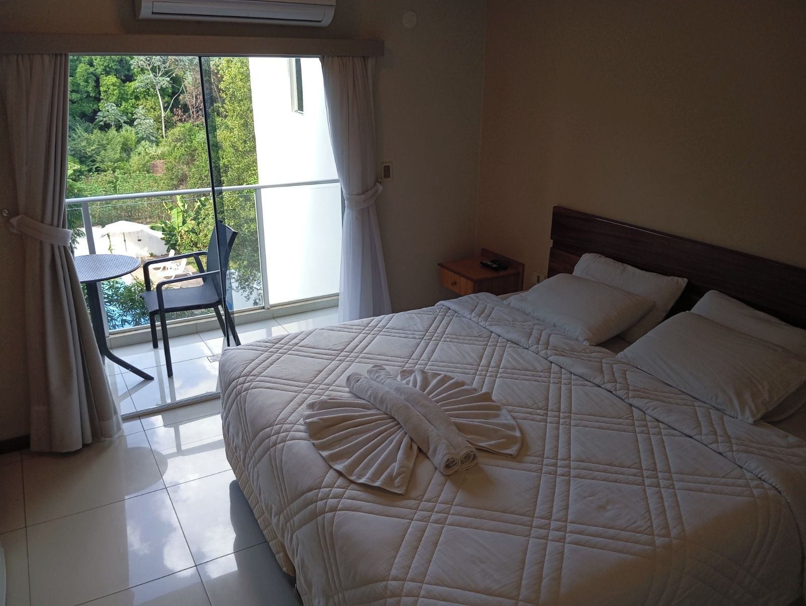 Habitación de hotel con una cama, una mesita de noche, una silla y vista a una piscina.