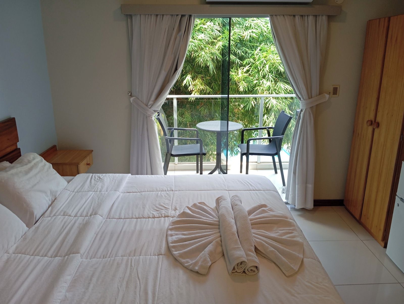 A hotel room with a bed, a balcony with a table and chairs, and a wardrobe.
