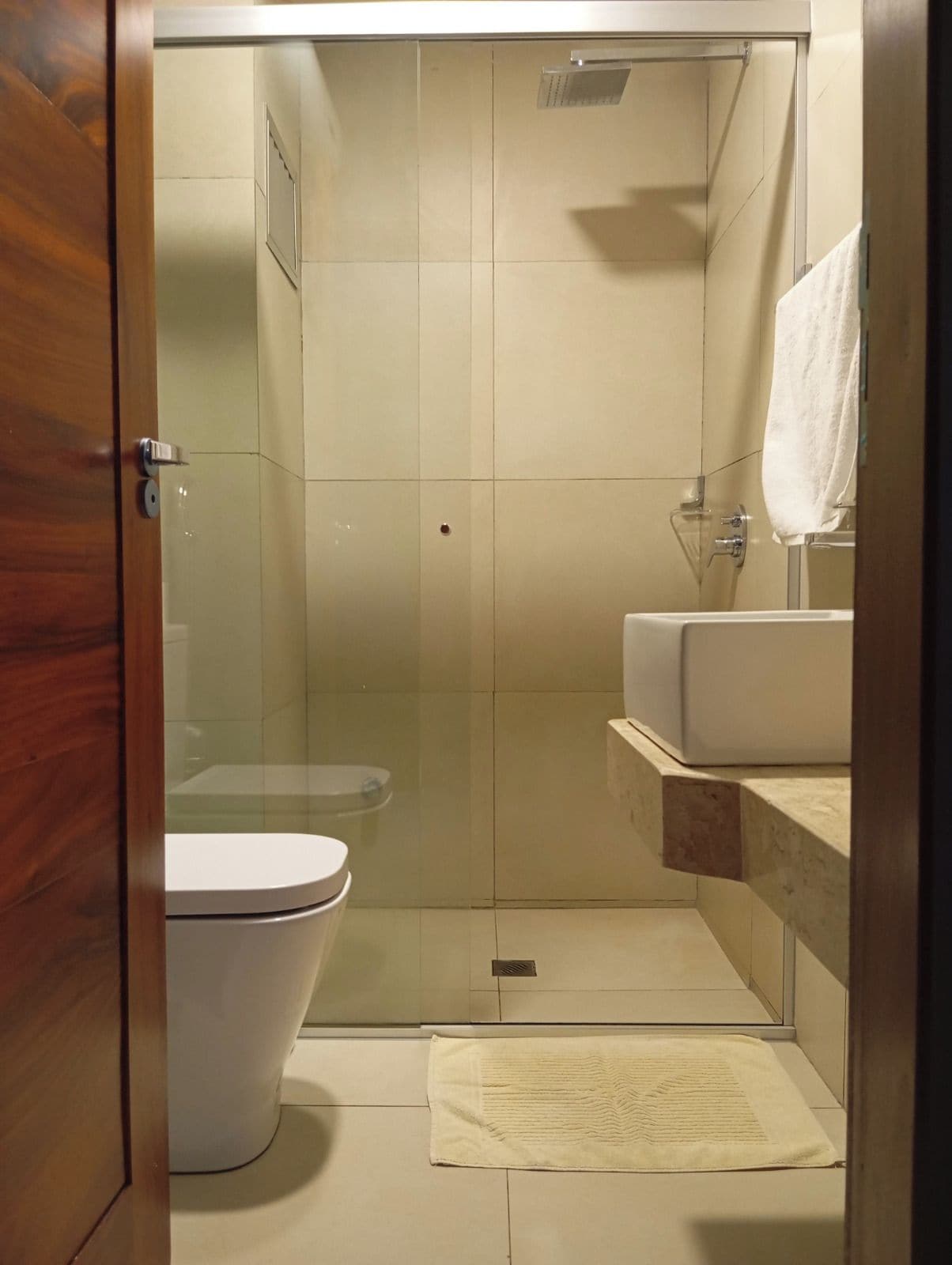 A bathroom with a glass-enclosed shower, a toilet, and a sink with a towel hanging on the wall.