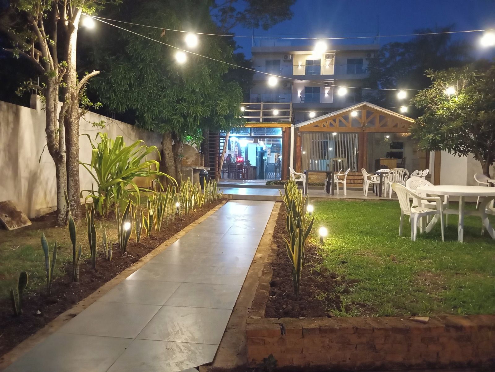 Un sendero exterior que conduce a un edificio con zona de restaurante, rodeado de vegetación y mesas al aire libre.