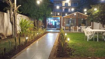 Un sendero exterior que conduce a un edificio con zona de restaurante, rodeado de vegetación y mesas al aire libre.