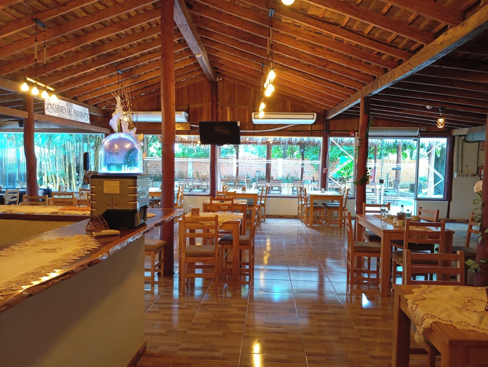 A restaurant with wooden furniture, a bar area, and large windows offering a view of the outdoors.