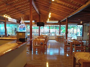 A restaurant with wooden furniture, a bar area, and large windows offering a view of the outdoors.