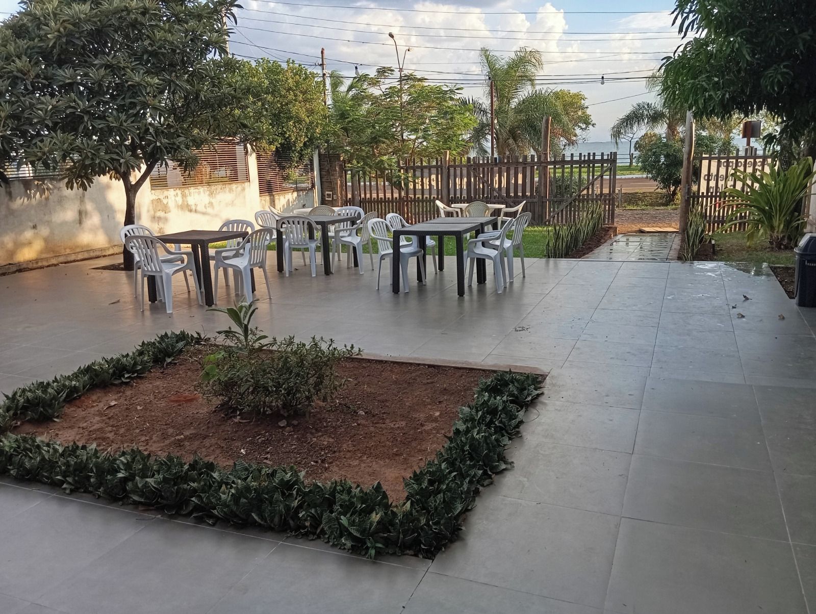 Un espacio al aire libre con mesas y sillas, rodeado por un muro de ladrillo bajo y una cerca de madera.