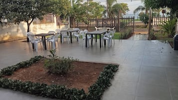 Un espacio al aire libre con mesas y sillas, rodeado por un muro de ladrillo bajo y una cerca de madera.