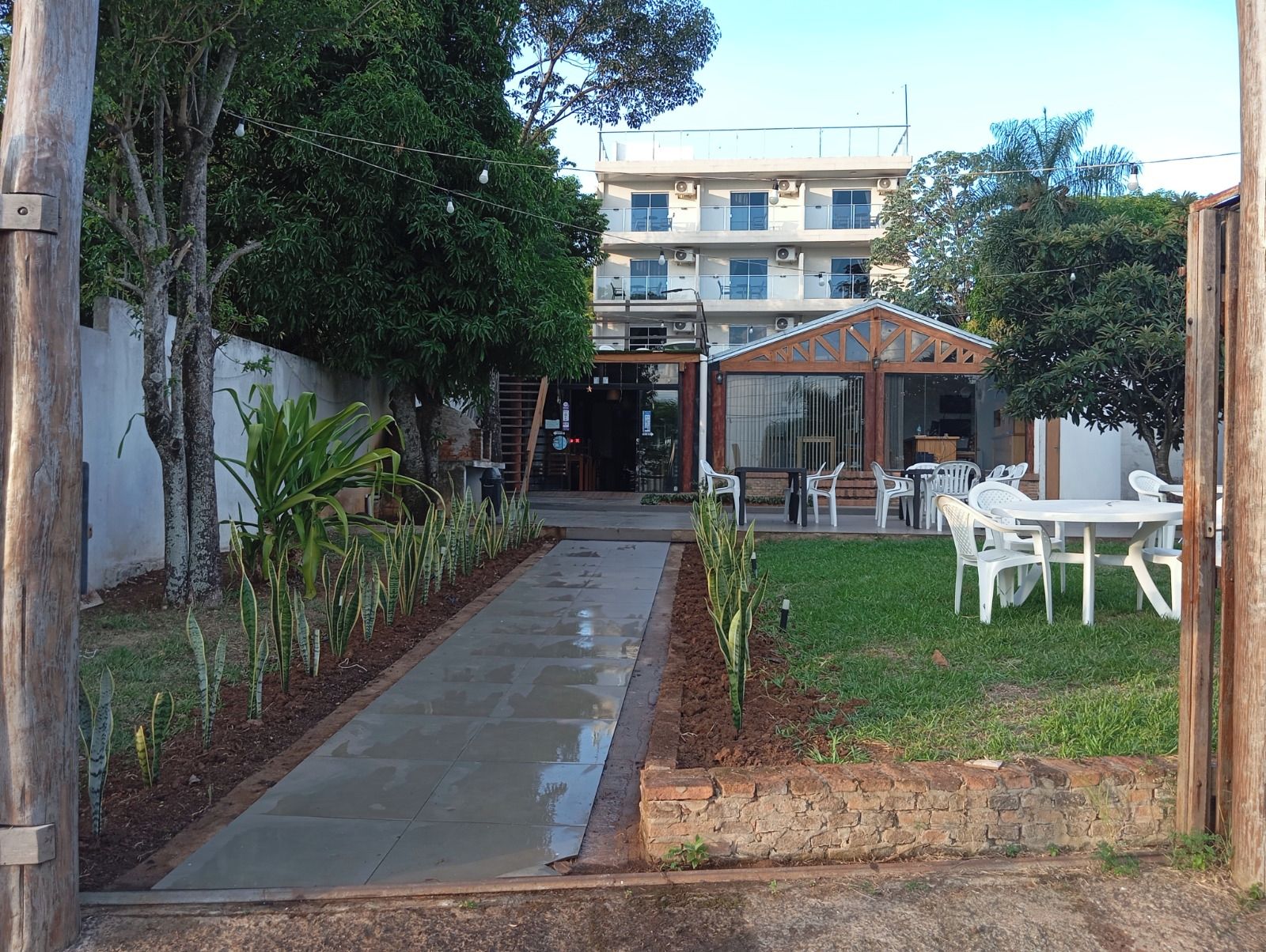 Un sendero conduce a un edificio con un área de estar al aire libre cubierta y un césped.
