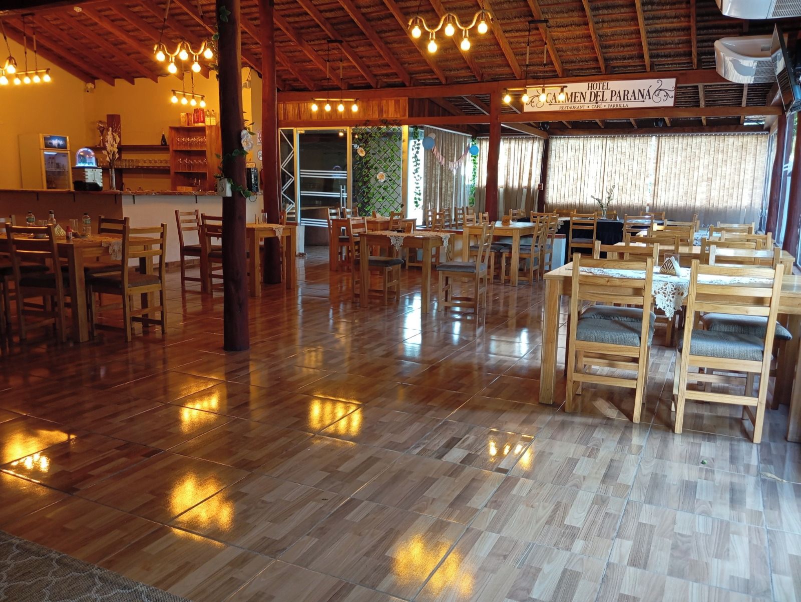 Ein Restaurant mit Holztischen und -stühlen, einem Fliesenboden und hängenden Lampen.