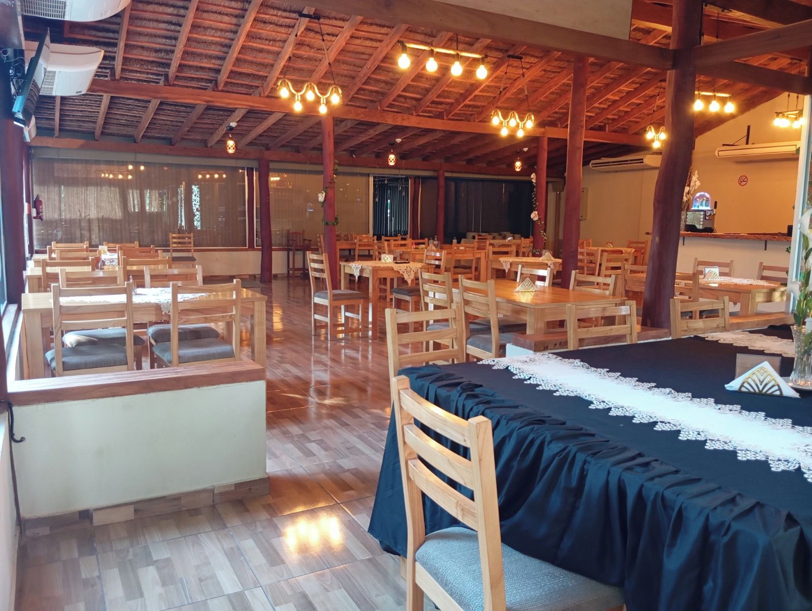 Un restaurante con mesas y sillas de madera, techo de paja y lámparas colgantes.
