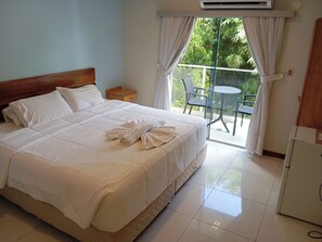 Una camera d'albergo con un letto, un comodino, un tavolo con sedie e vista sul verde attraverso la finestra.