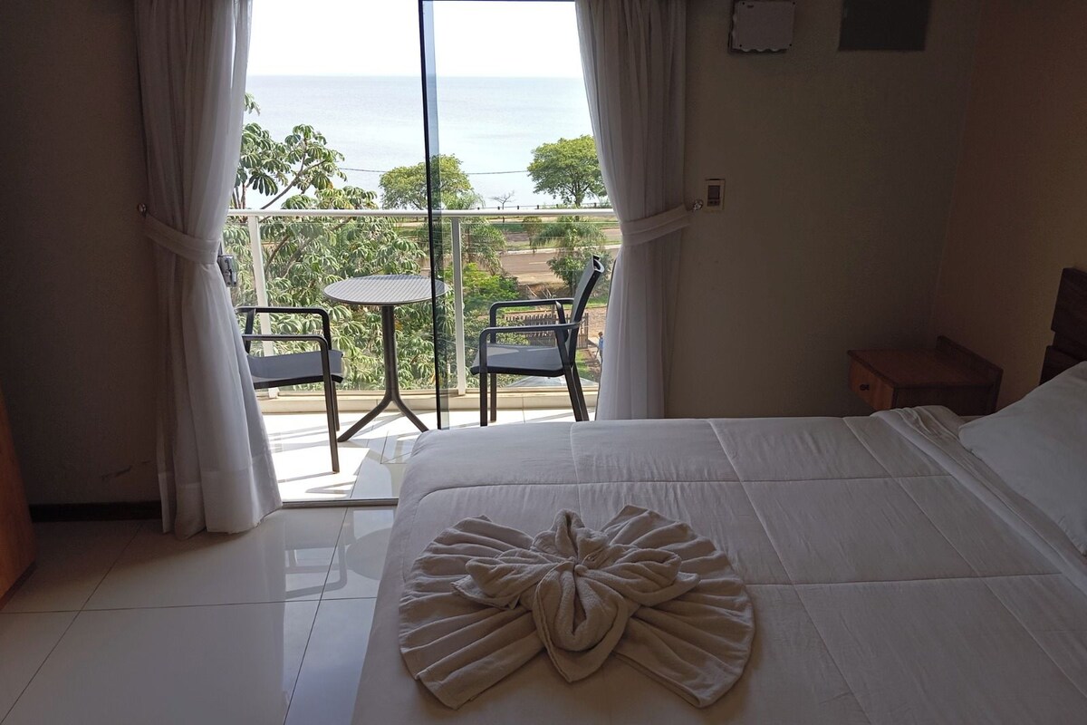 Una camera d'albergo con un letto, un tavolo, sedie e vista sul mare.