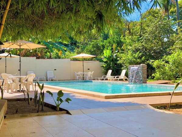 A swimming pool with lounge chairs and umbrellas, surrounded by greenery.