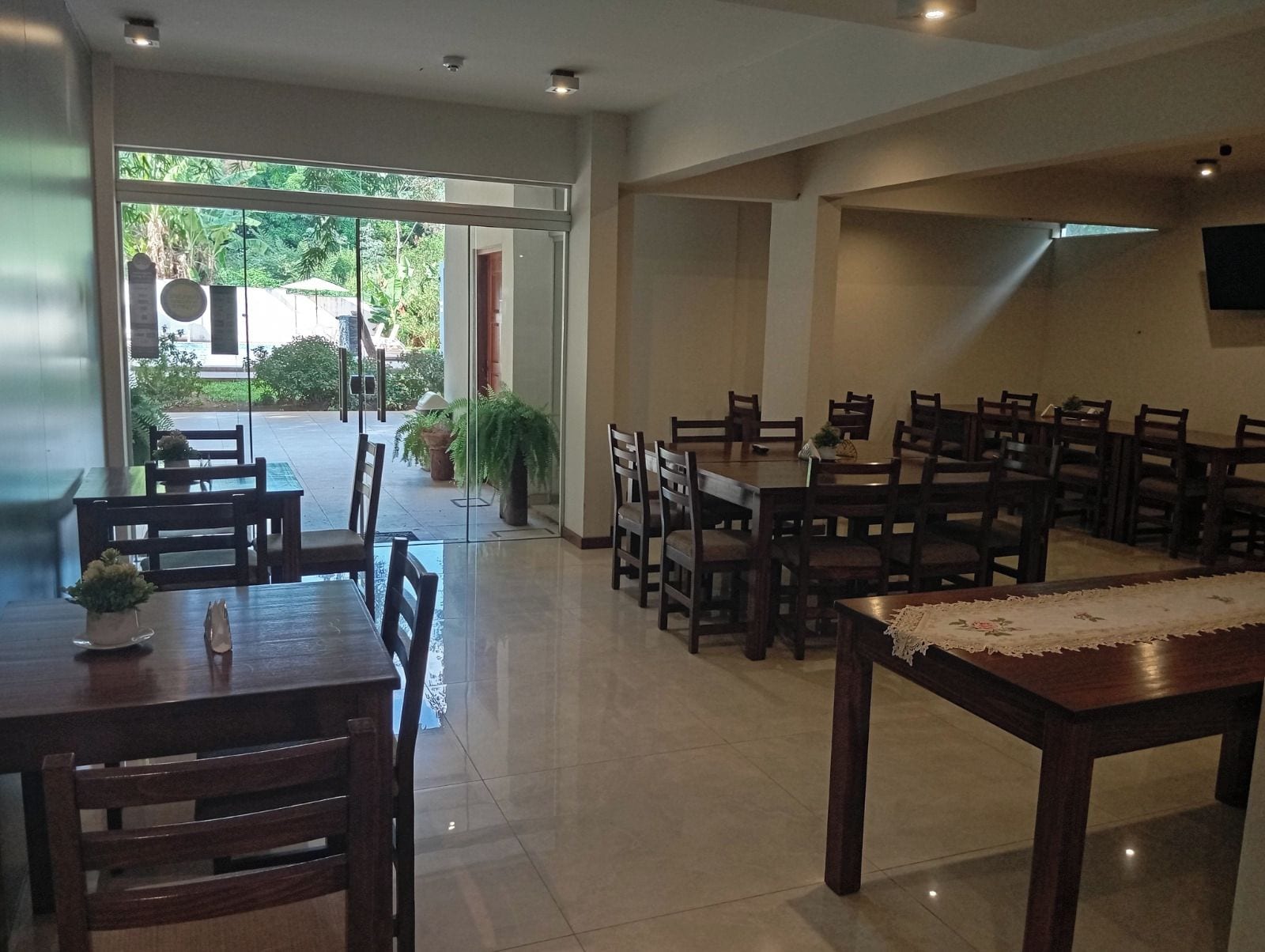 A dining area with multiple tables and chairs, a glass door leading outside, and a tiled floor.