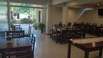 A dining area with multiple tables and chairs, a glass door leading outside, and a tiled floor.