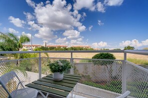 Ein Balkon mit Tisch und Stühlen, einem Blumentopf und Blick auf ein Gebäude und eine Windmühle in der Ferne.