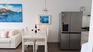 Een moderne keuken met een roestvrijstalen koelkast, een eettafel met stoelen en een witte bank.