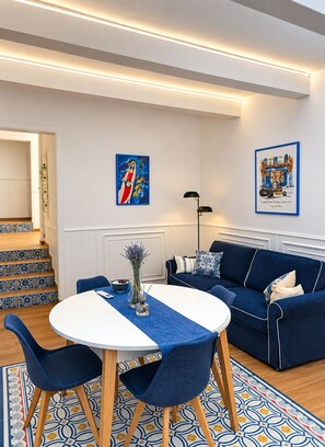 A modern living room with a blue sofa, a round table, and a staircase with patterned tiles. - The advantages of a detached house with services and quality of a boutique hotel (Il-Belt Valletta)