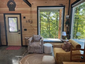 A cozy room with a wooden interior, a door with a window, a patterned armchair, a round ottoman, and a sofa with a cushion. - Charming, secluded bungalow in the Mountain View area. (Mountain View)