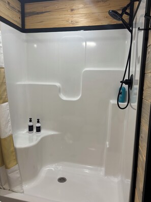 A shower with a wooden ceiling, a drain, and two bottles of shampoo on a shelf. - Charming, secluded bungalow in the Mountain View area. (Mountain View)