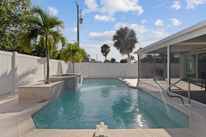 A swimming pool with a tiled edge, a palm tree, and a white fence. - Beachside Oasis (Fort Myers Beach)