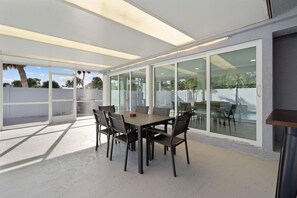A covered patio area with a table and chairs, large sliding glass doors, and a view of the outdoors. - Beachside Oasis (Fort Myers Beach)