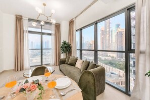 Een moderne woonkamer met een eethoek, grote ramen met uitzicht op de stad, en een groene bank.