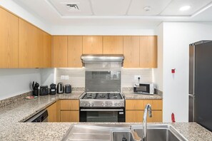 Una cocina moderna con armarios de madera, una campana extractora de acero inoxidable, estufa a gas, microondas y refrigerador.