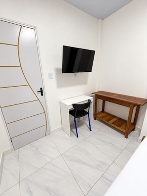 Une pièce avec une porte blanche, un bureau avec une chaise, un téléviseur fixé au mur et une table en bois.