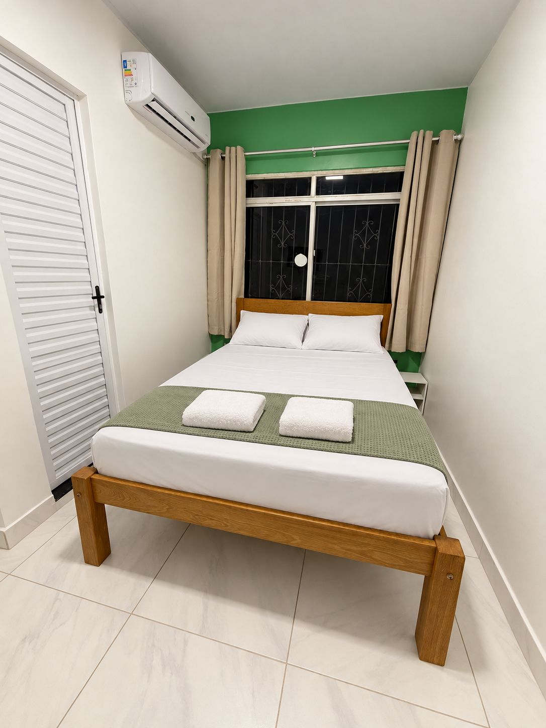 Een slaapkamer met een bed, een raam met gordijnen, een airconditioning en een deur.
