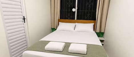A bedroom with a bed, a window with curtains, an air conditioning unit, and a door.