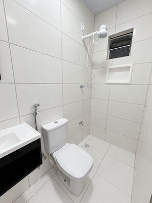 Une salle de bain avec des toilettes, un lavabo, une douche et une petite fenêtre.