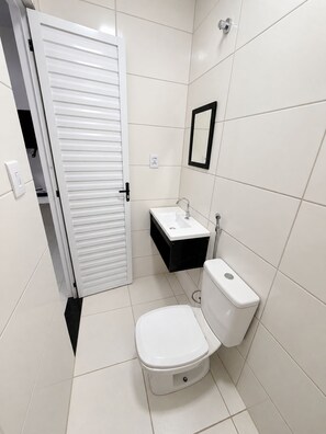 A small, modern bathroom with a toilet, sink, and mirror. - Casa verde com Wi-Fi 700MB e ãgua quente (Belém)