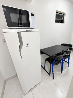 A compact kitchenette with a refrigerator, microwave, and a small window for ventilation. - Casa verde com Wi-Fi 700MB e ãgua quente (Belém)
