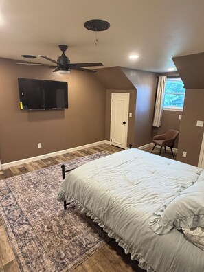 Une chambre dotée d’un ventilateur de plafond, d’un téléviseur à écran plat, d’un lit avec un tapis à motifs et d’une fenêtre avec des rideaux.