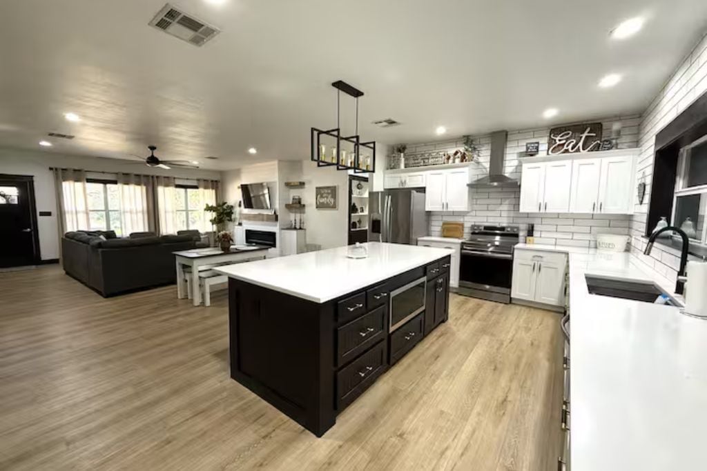 Una cocina moderna con una isla grande, armarios blancos y un comedor con sofá y mesa.