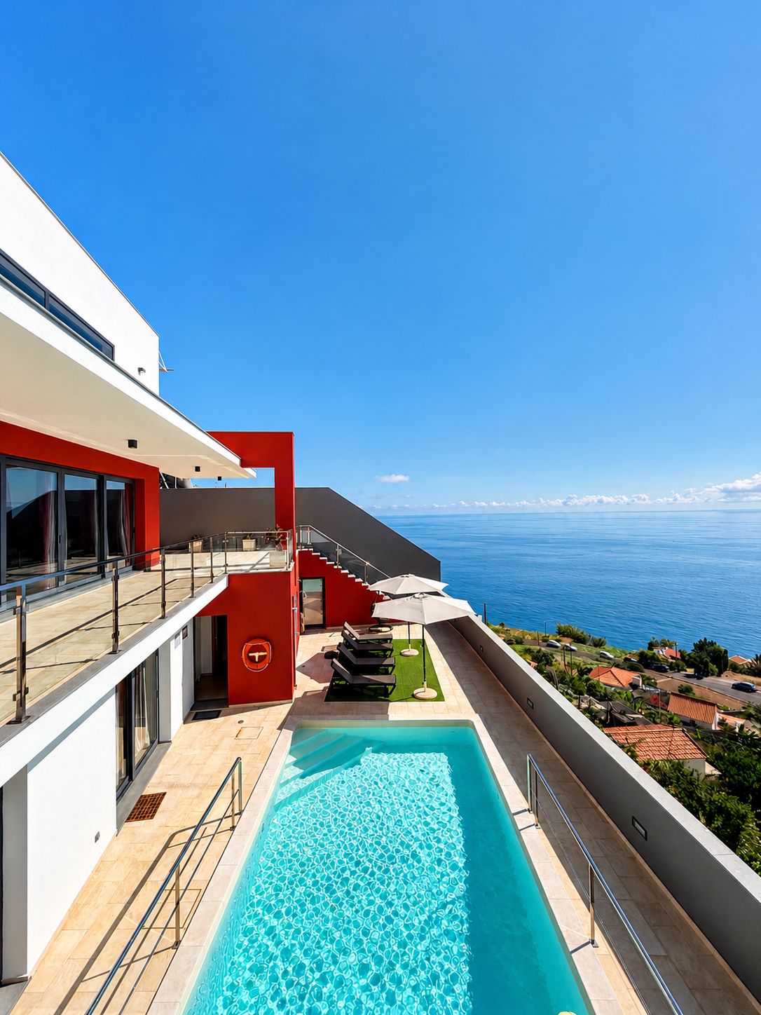 A modern building with a pool, a staircase, and a view of the sea.