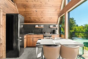 A compact kitchen with wooden cabinets, a black refrigerator, and a dining area with two chairs. - Kate's Luxury TreePod | Smoky Mountains (Sevier County)