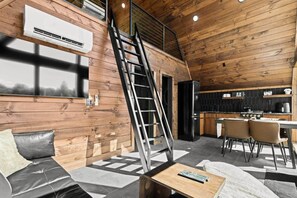 A cabin interior with a loft bed, a kitchen area, and a dining space. - Kate's Luxury TreePod | Smoky Mountains (Sevier County)
