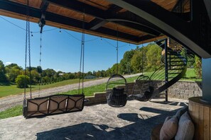 A covered outdoor seating area with a swing, chairs, and a spiral staircase. - Kate's Luxury TreePod | Smoky Mountains (Sevier County)