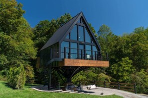 Et moderne træhus med stor balkon, omgivet af frodigt grønt.