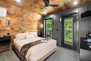 A bedroom with a bed, a ceiling fan, a bedside table, a nightstand, and a view of the outdoors through a door. - Kate's Luxury TreePod | Smoky Mountains (Sevier County)