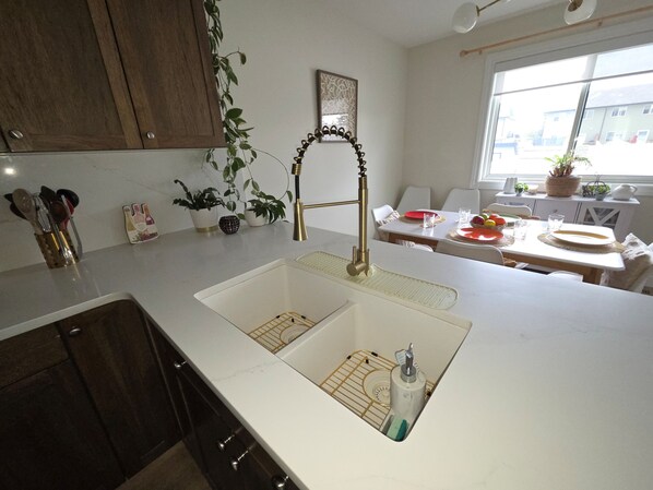 A modern kitchen with a white countertop, a gold faucet, and a sink with a soap dispenser. - The ultimate lake getaway awaits! (Sylvan Lake)