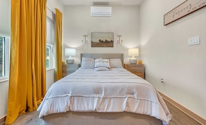 A bedroom with a bed, two bedside tables, a wall-mounted air conditioner, a painting, and a sign on the wall. - Casa Serena + Boat Parking+ Fire Pit +Walk to lake (Belton)