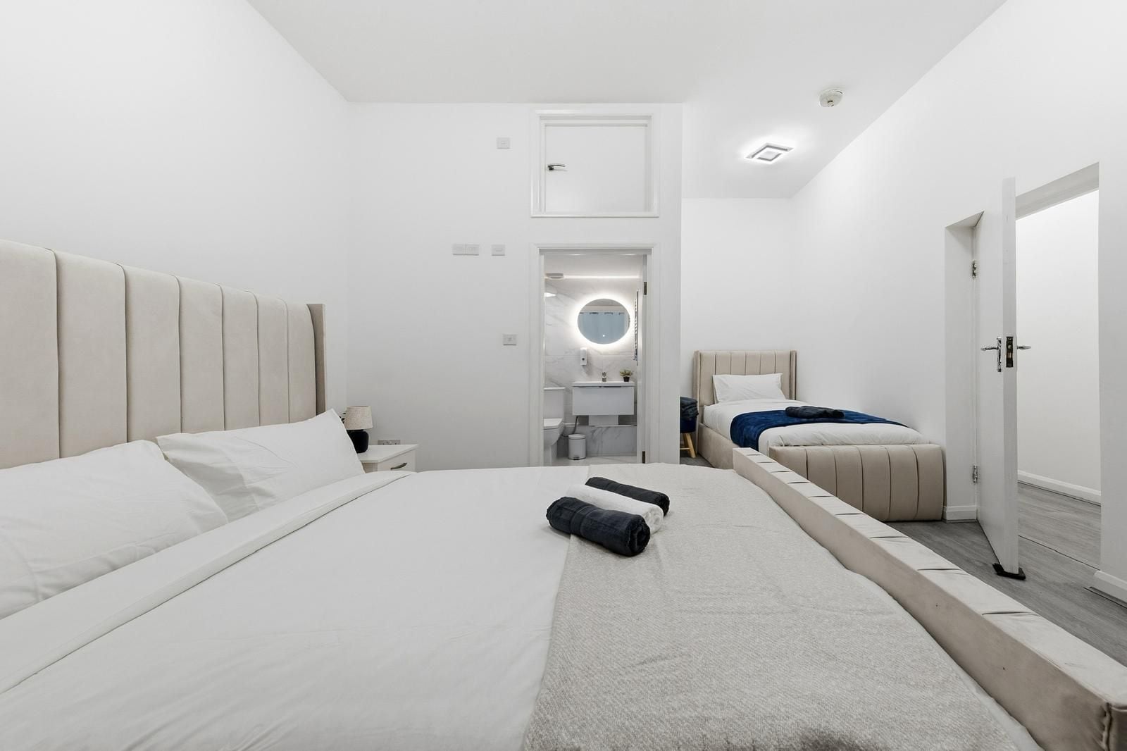 A modern hotel room with two beds, a small bathroom, and a view of the city.