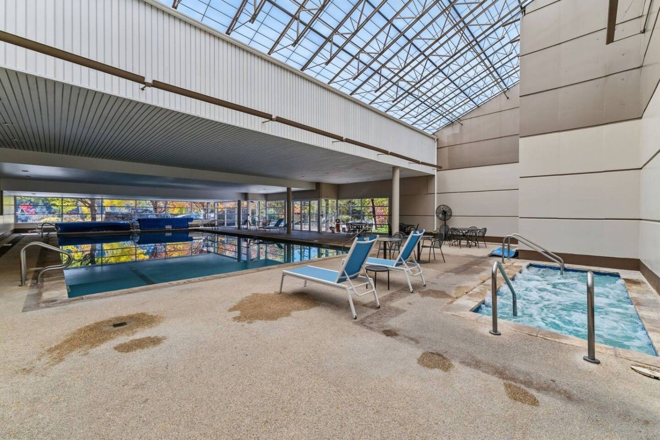 Una piscina interna con tetto in vetro, poltrona relax e vista sugli alberi esterni.