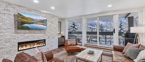 A modern living room with a fireplace, leather sofas, a coffee table, and a large TV mounted on a stone wall.